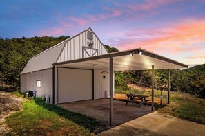 A barn with a covered outdoor area, a picnic table, and a large garage door. - Big Fern | Pet-Friendly Cabin Near Frio & Garner (Leakey)