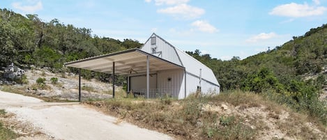 A single-story building with a covered porch and a garage door, surrounded by natural landscape and a dirt road.