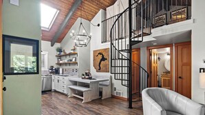 A spacious kitchen with wooden flooring, a dining area with a bench, a staircase, and a large window. - Townhouse in Private Lakeside Community (Sandpoint)