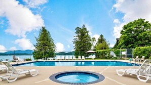 A swimming pool with lounge chairs and a hot tub, surrounded by trees and a view of a lake. - Townhouse in Private Lakeside Community (Sandpoint)