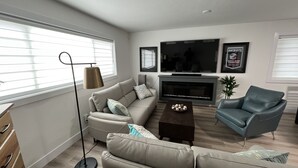 Een moderne woonkamer met een bank, fauteuil, salontafel en een flatscreen televisie aan de muur.