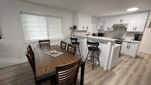 Een moderne keuken met witte kasten, een houten eettafel en barstoelen.