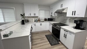 Een moderne keuken met witte kastjes, een magnetron, een kookplaat en een koffiezetapparaat.