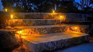 Escaleras de piedra al aire libre con iluminación integrada, rodeadas de árboles y un cielo despejado.