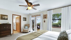 Un dormitorio con cama, ventilador de techo, cómoda y puerta que da a un balcón.