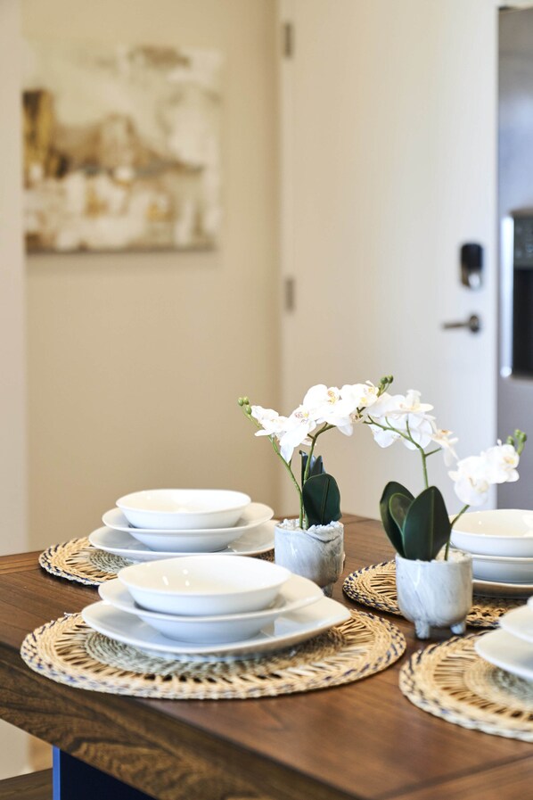 Una mesa de comedor con platos blancos, cuencos y protectores de mesa tejidos.