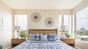 Une chambre dotée d’un grand lit, de deux œuvres d’art murales, d’une tête de lit en bois, de deux tables de chevet avec des lampes et offrant une vue sur la ville grâce à de grandes fenêtres.
