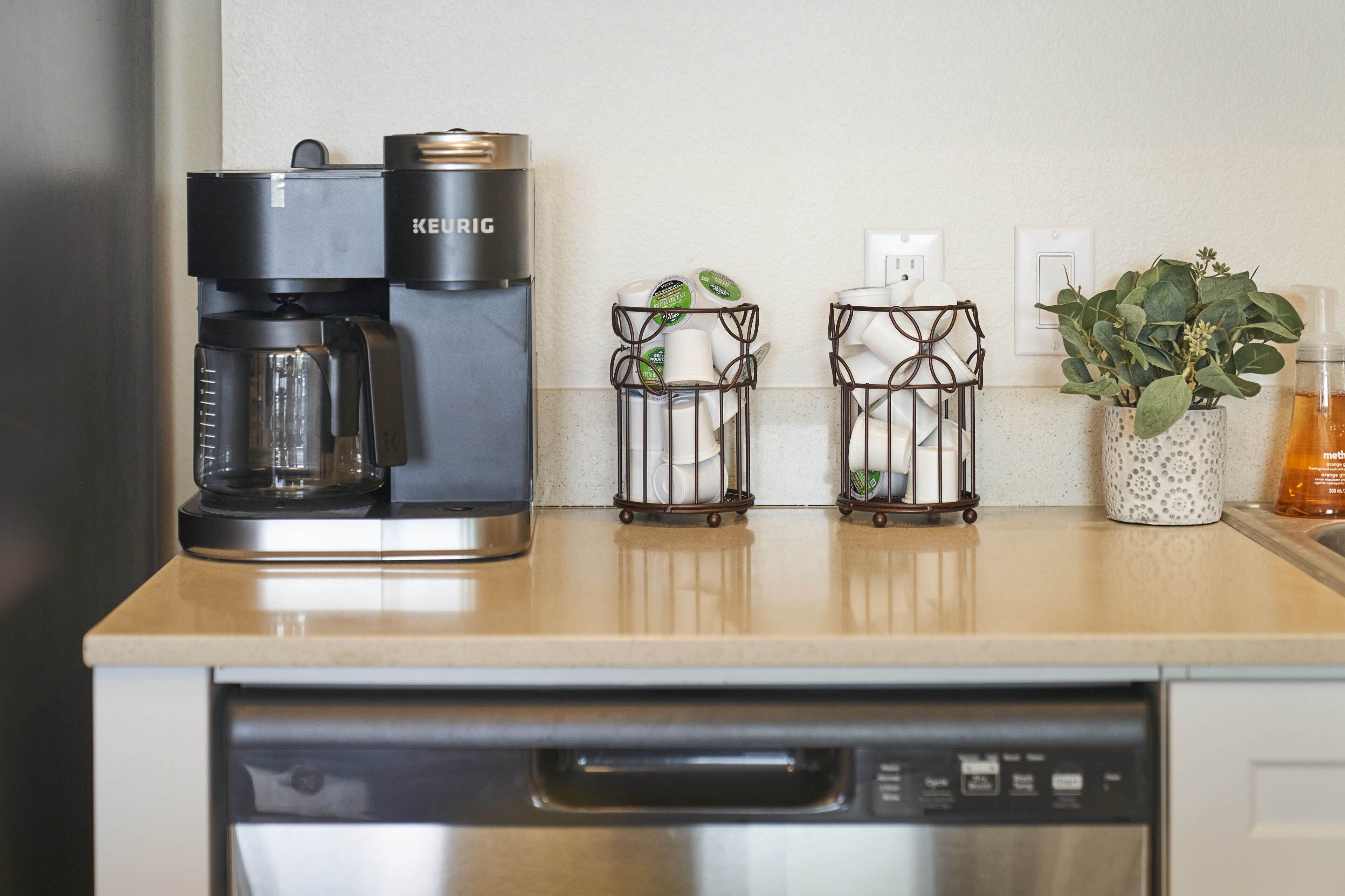 A kitchen counter with a Keurig coffee maker, two candle holders, a potted plant, and a soap dispenser.