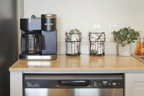 Una cuina amb un taulell, una cafetera Keurig, dos suportes per a espelmes, una planta en test i un dosificador de sabó.