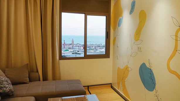 A room with a large window, a sofa, and a wall with abstract art. - Anza Beach View Apartment (Agadir)