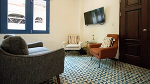Een kamer met een vloer met patroon, twee fauteuils, een televisie en een deur.