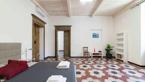 Ein Hotelzimmer mit einem Bett, einem Sessel, einem kleinen Tisch mit einer Pflanze und einem Wandregal.