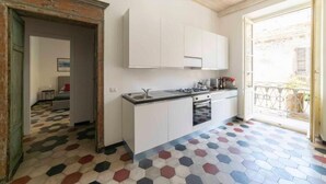 Eine Küche mit weißen Schränken, einem Herd und einem Spülbecken. Der Boden ist mit farbenfrohen, sechseckigen Fliesen ausgelegt und es gibt einen Balkon mit einem Metallgeländer.