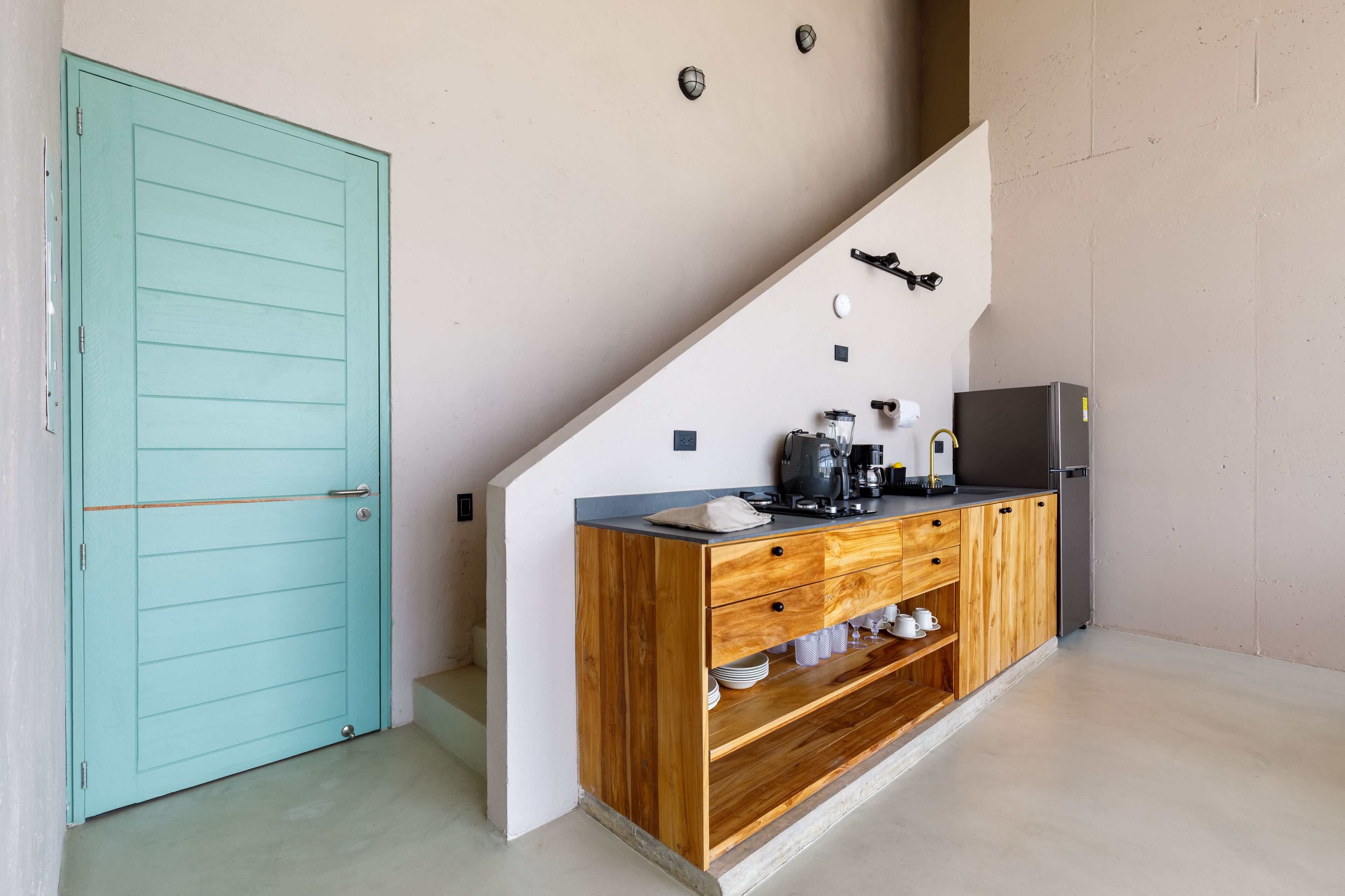 Cozinha com porta verde-água, armários de madeira e bancada com cafeteira e xícaras.