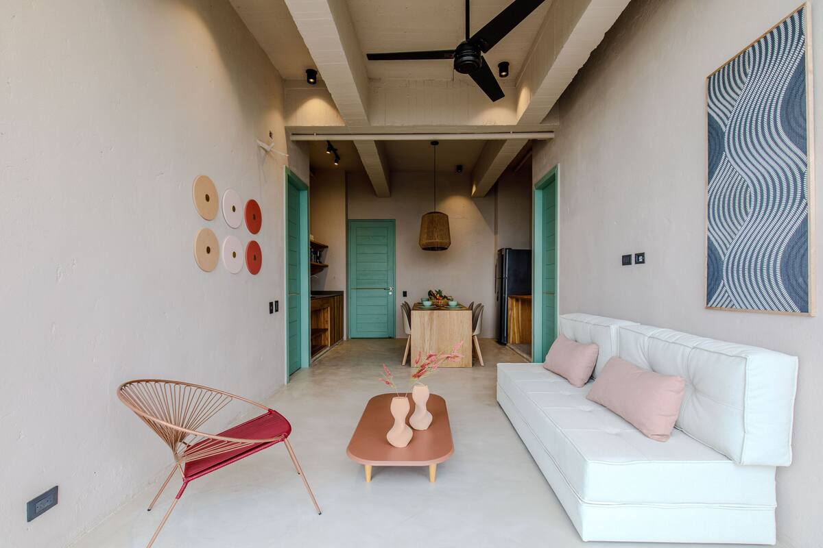 A modern living room with a white sofa, a red chair, and a coffee table with vases. There is a ceiling fan and a painting on the wall.