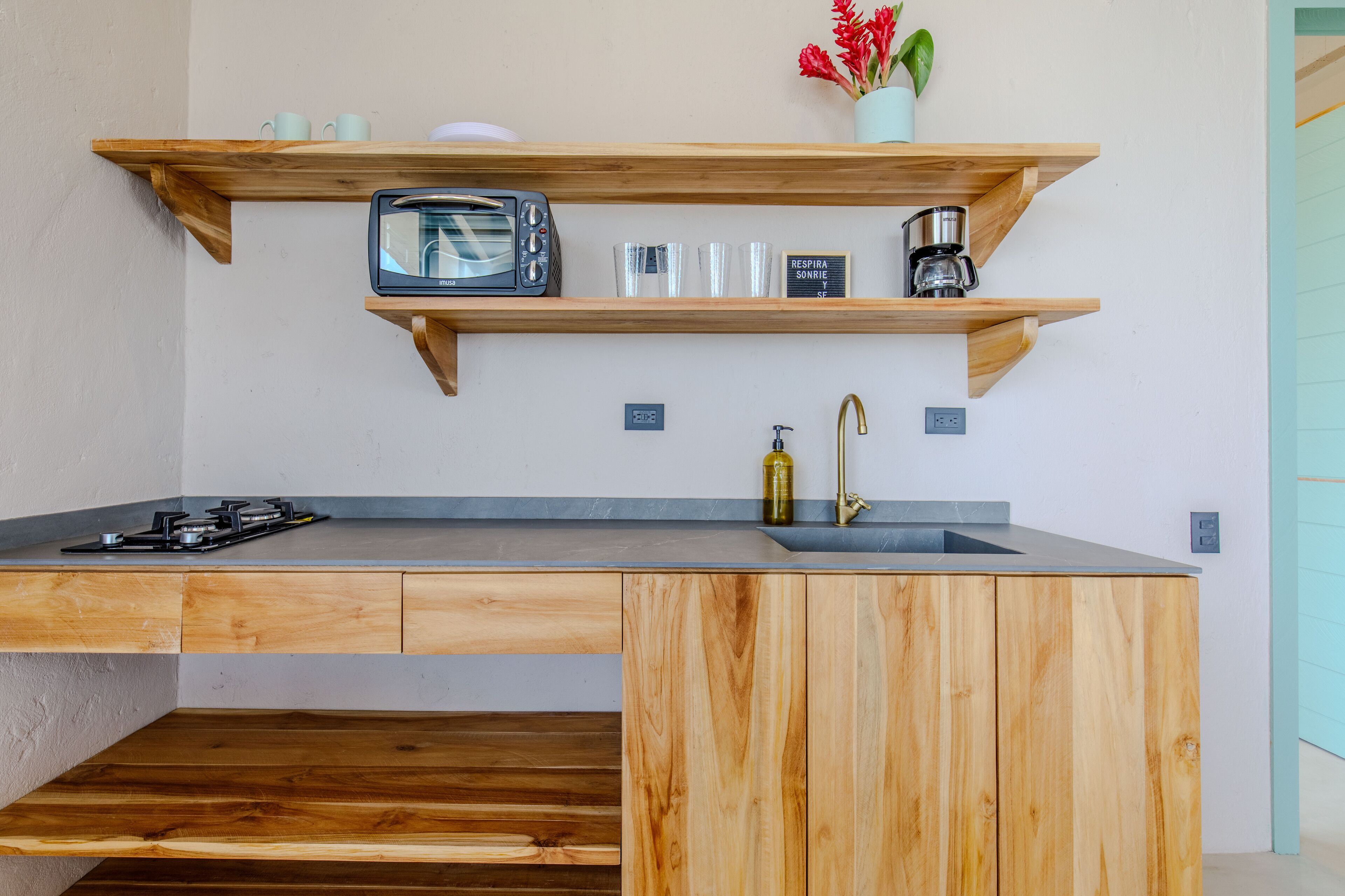 A modern kitchen with wooden shelves, a microwave, a coffee maker, and a sink.