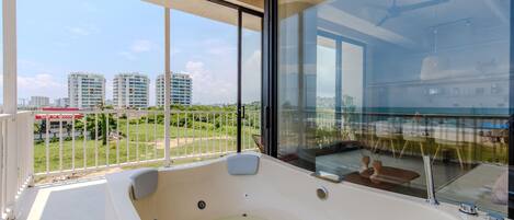 A modern balcony with a hot tub, large windows, and a view of city buildings.