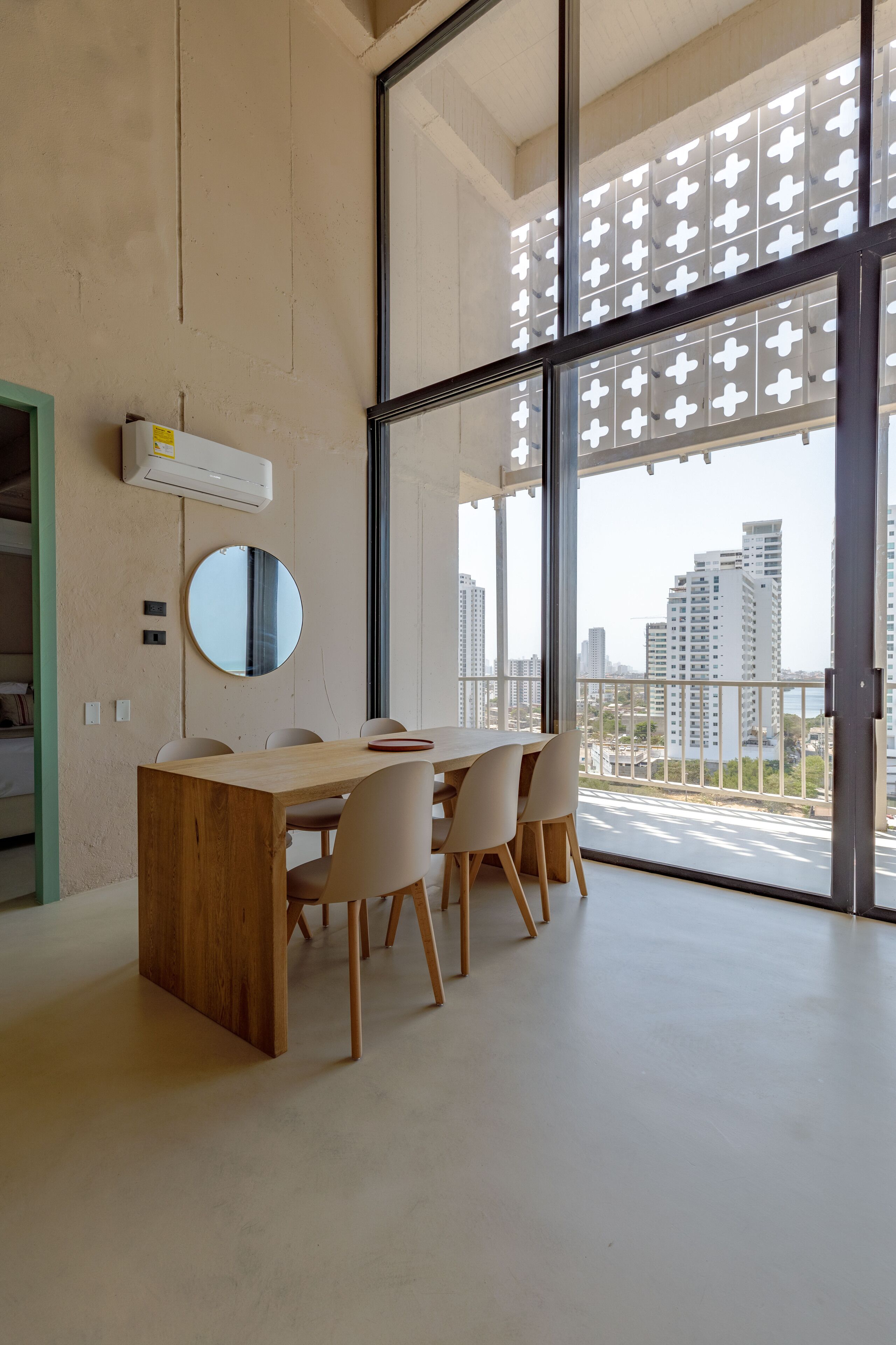 Ein moderner Essbereich mit Holztisch und -stühlen, einem runden Spiegel und großen Fenstern mit Blick auf die Stadt.