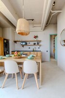 A modern kitchen with a wooden dining table, white chairs, and a hanging light fixture.