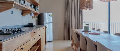 A modern kitchen with wooden cabinets, a stainless steel refrigerator, and a dining area with a long table and chairs.