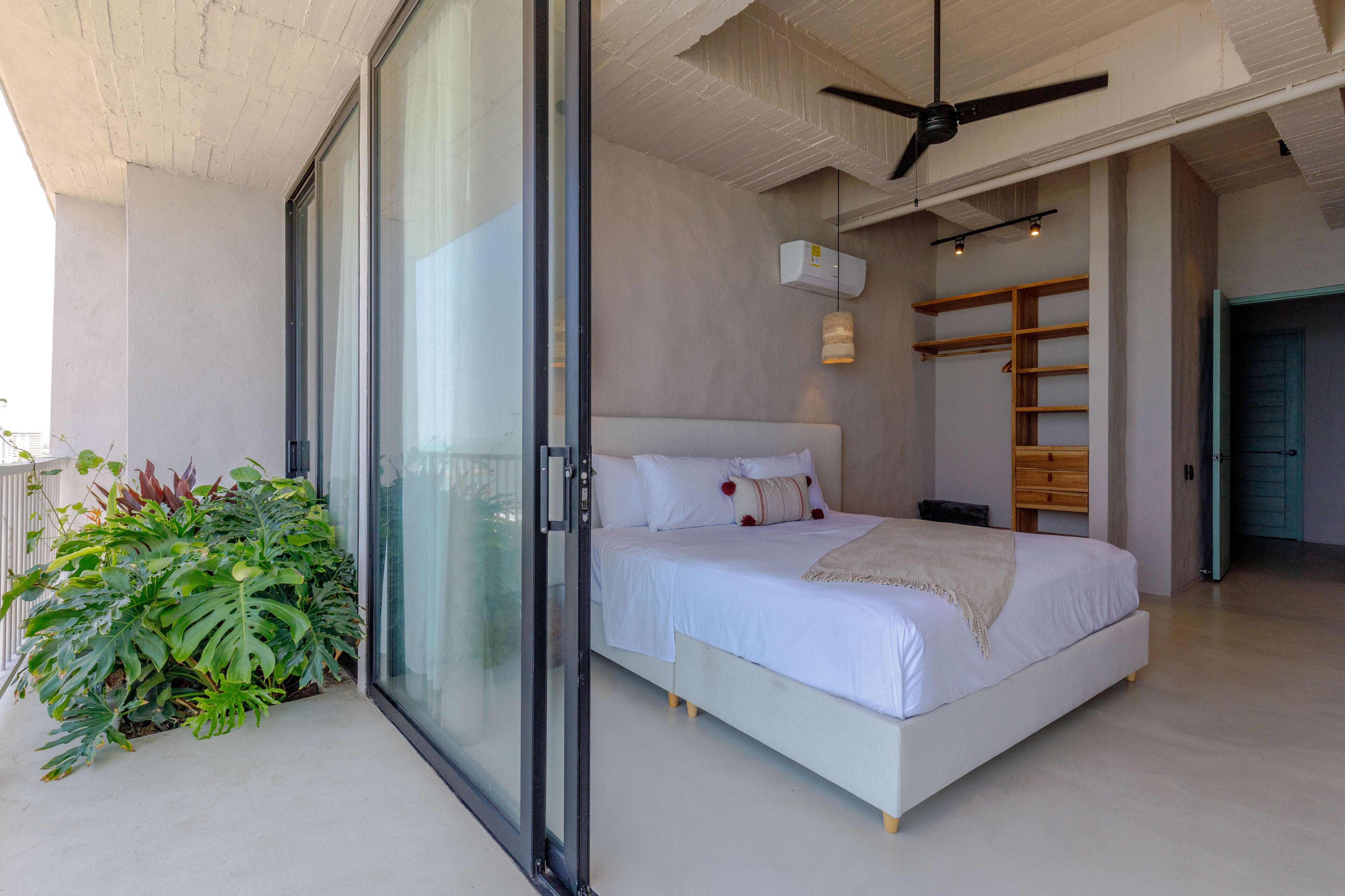 A bedroom with a bed, a ceiling fan, a window, and a plant.