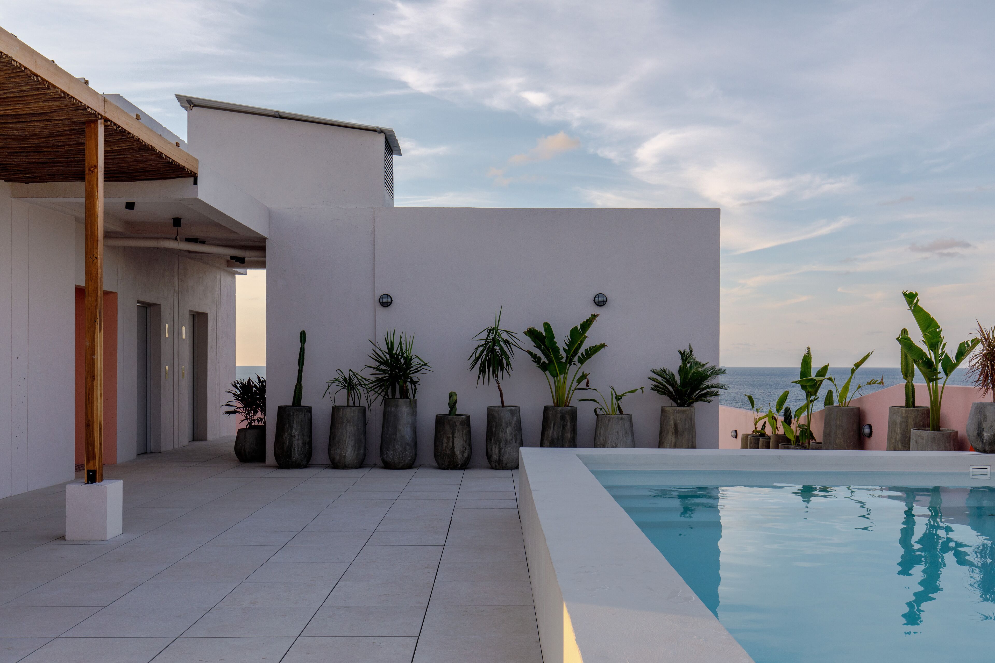 A modern pool area with a clear view of the sea, surrounded by potted plants and a minimalist architectural design.