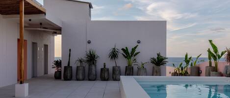 A modern pool area with a clear view of the sea, surrounded by potted plants and a minimalist architectural design.