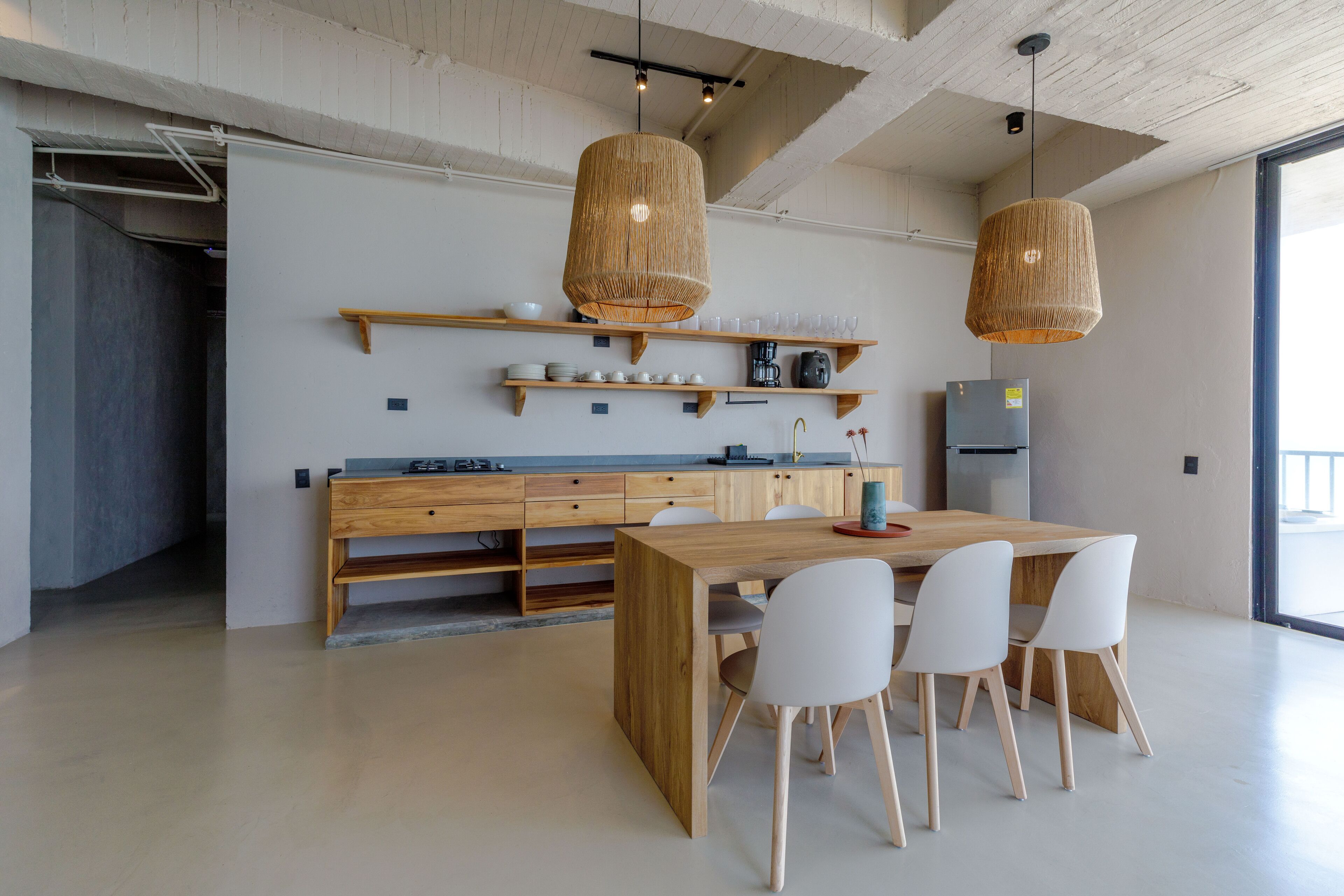 Una cocina moderna con armarios de madera, una isla central, sillas blancas y dos lámparas colgantes de mimbre.