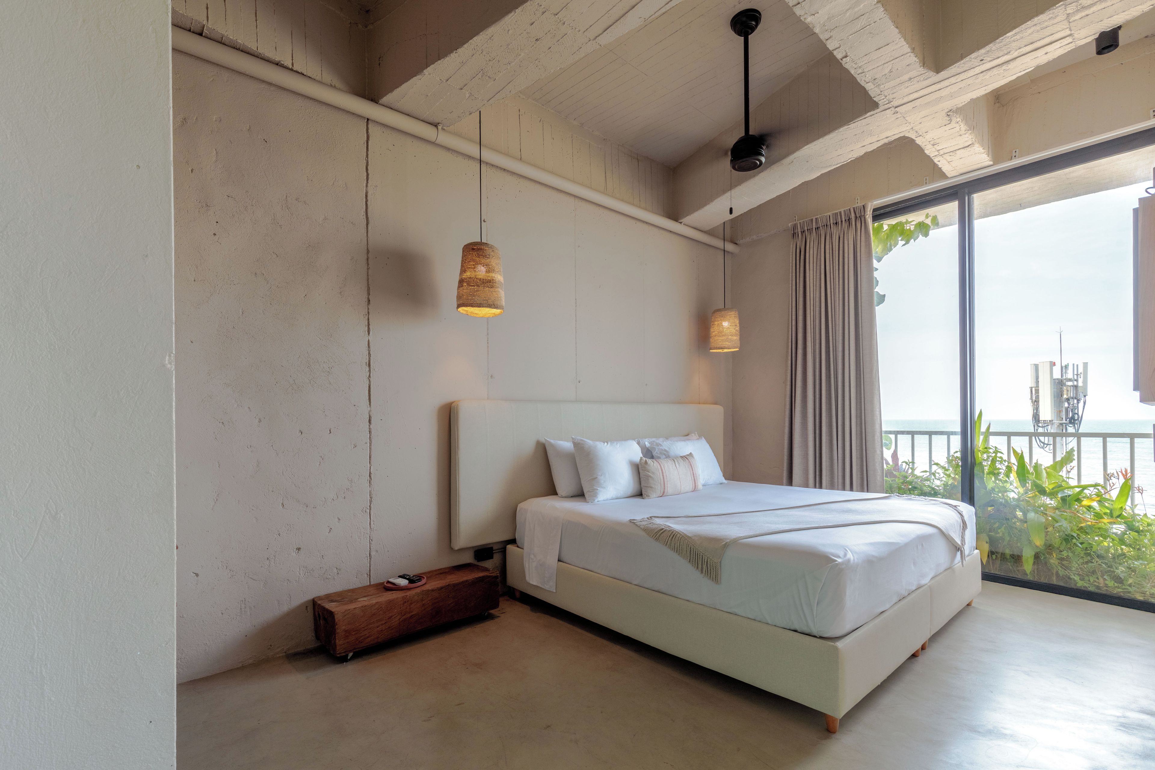 Un dormitorio con una cama grande, una mesita de noche de madera y vistas al mar desde un balcón.