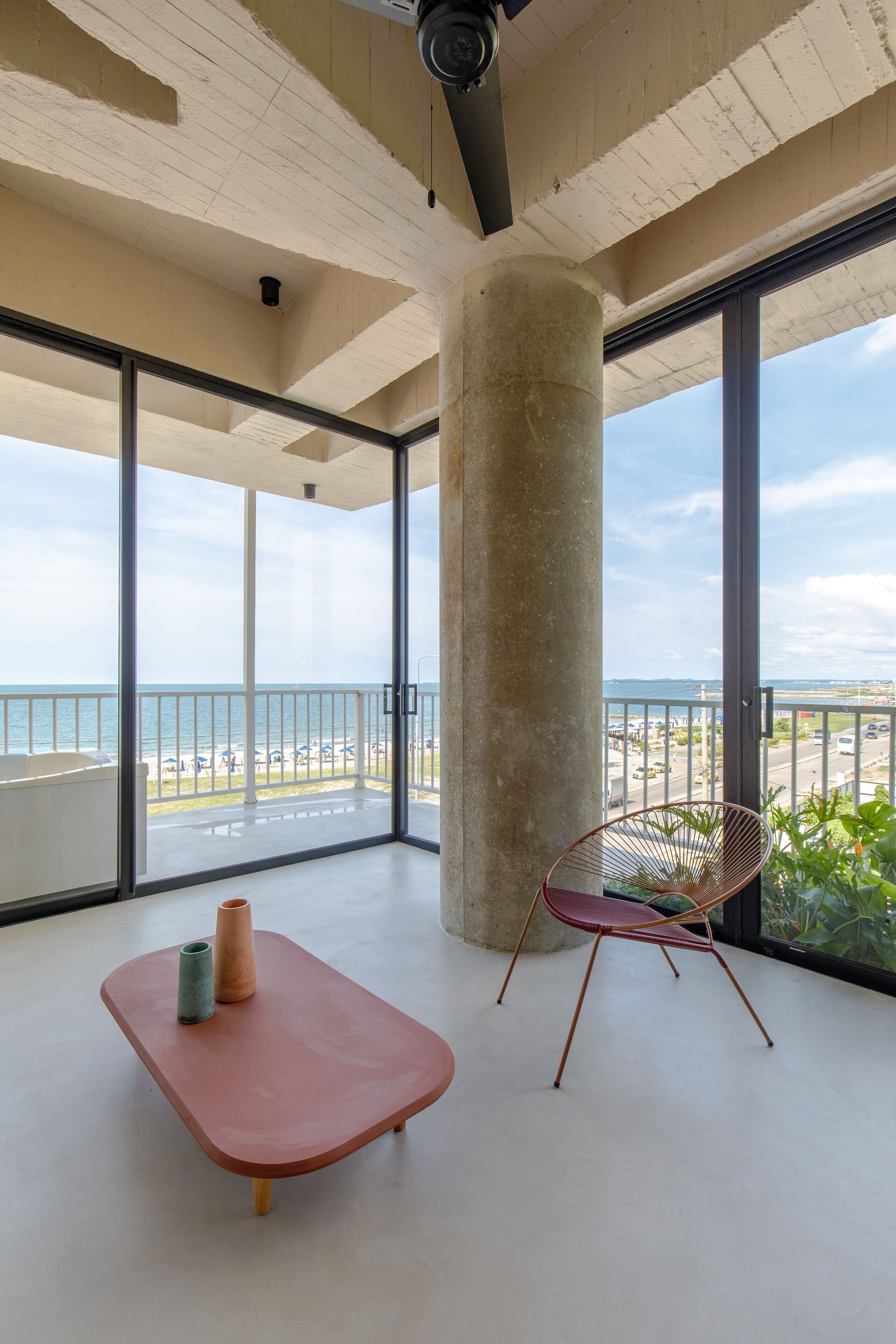 A spacious balcony with a concrete pillar, a red chair, and a small table with two vases.