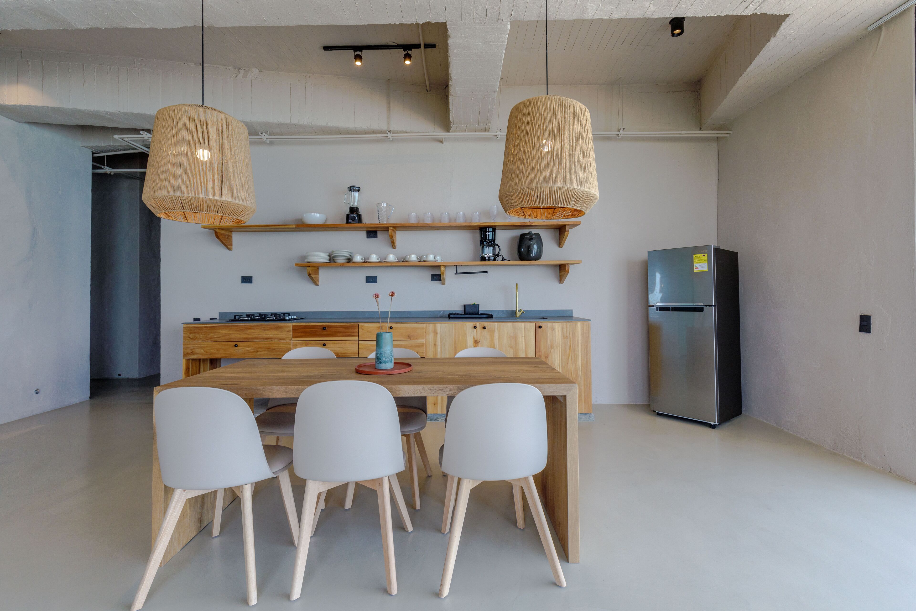 A modern kitchen with a wooden island, white chairs, and hanging wicker pendant lights.
