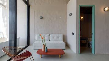 A modern living room with a white sofa, a red coffee table, and a wicker chair.
