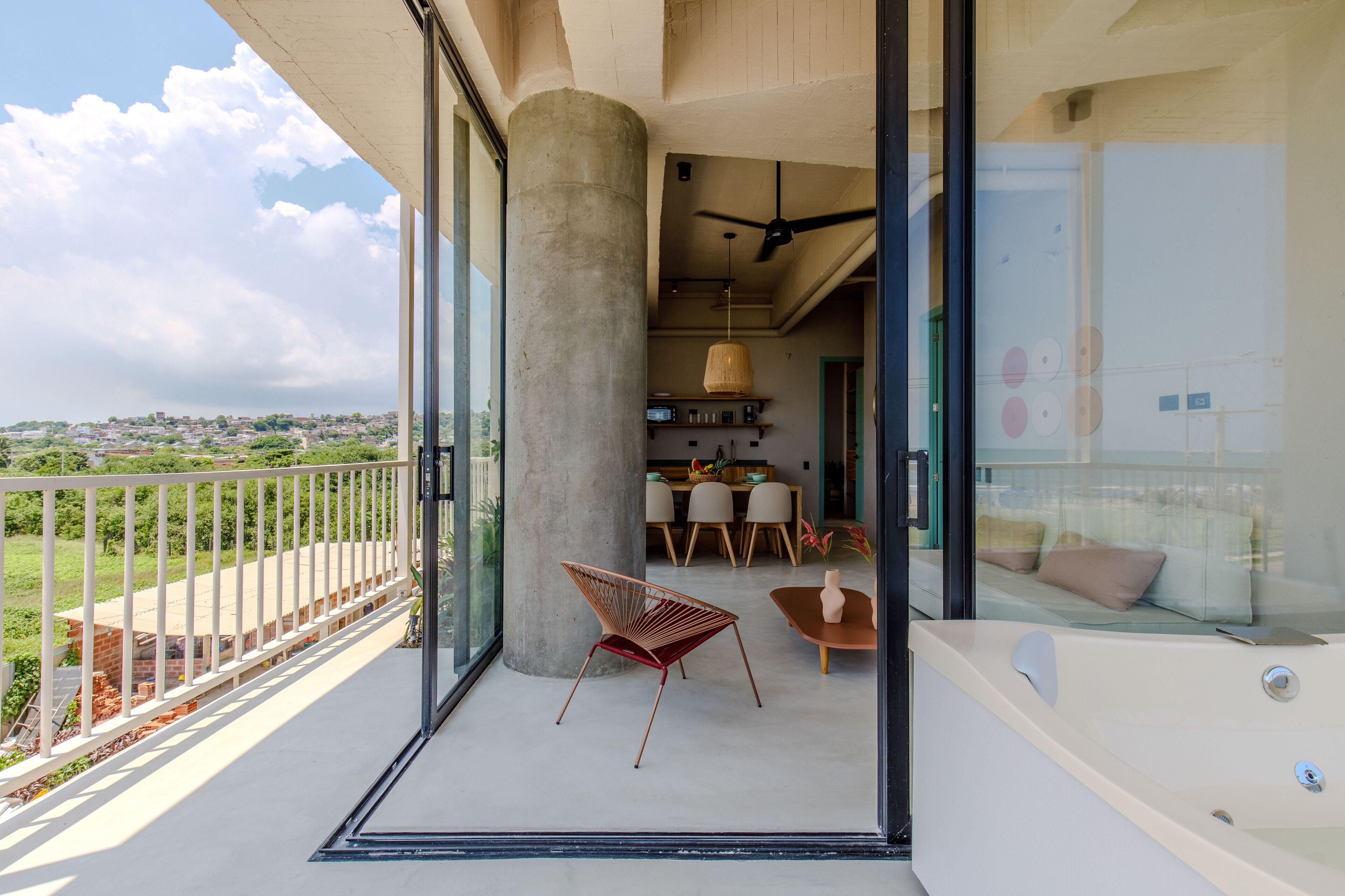 A balcony with a glass door leading to a dining area, a large pillar, and a hot tub.