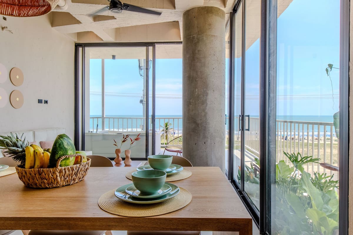 A modern dining area with a wooden table, chairs, and a view of the ocean.