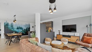 A modern living room with a large sofa, a dining table, and a kitchen area. - GebirgsResort Winterberg (Winterberg)