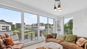 A spacious balcony with a leather chair, a brown sofa with decorative pillows, and a round wooden table with a white furry rug. - GebirgsResort Winterberg (Winterberg)
