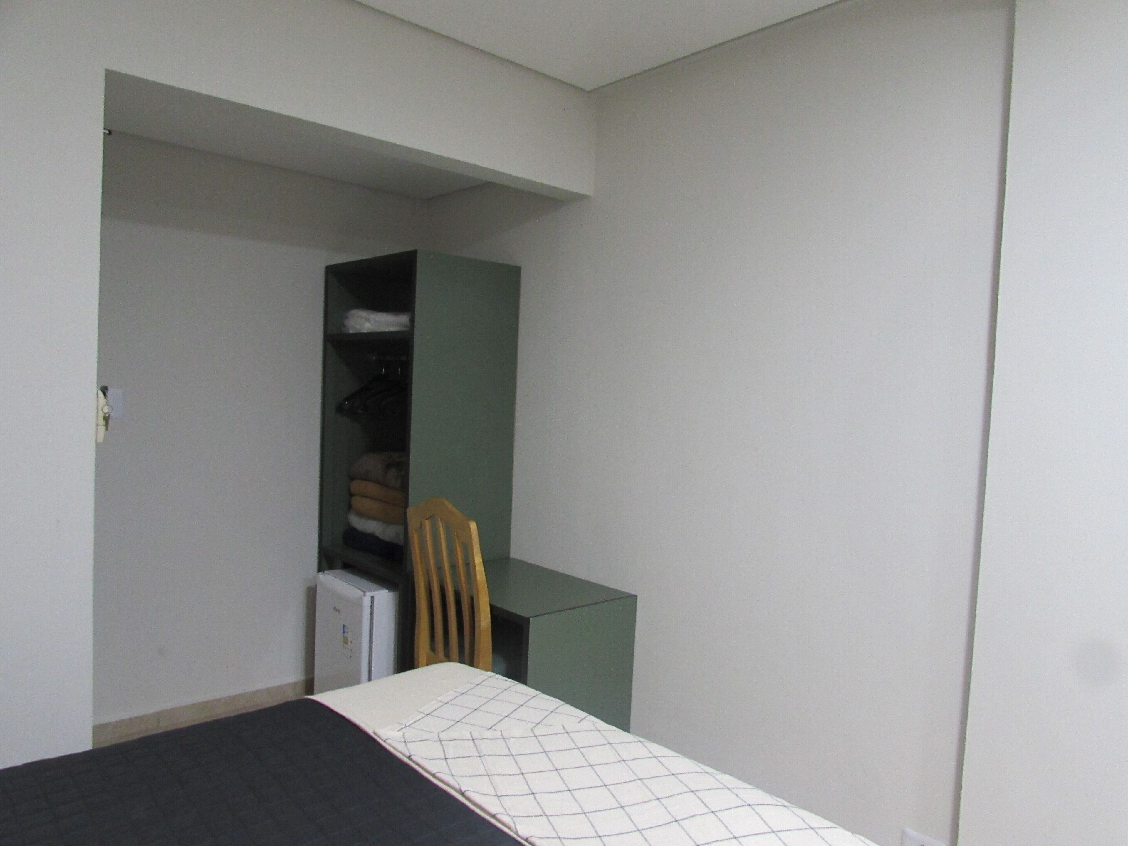 Una habitación pequeña y con pocos muebles, que contiene una cama, una silla, un escritorio y un armario.