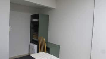 Una habitación pequeña y con pocos muebles, que contiene una cama, una silla, un escritorio y un armario.
