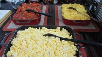 Une table de buffet proposant divers plats, notamment des œufs brouillés, des saucisses et du riz.