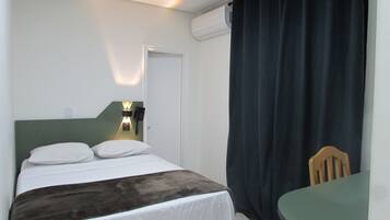 A hotel room with a bed, a desk, a chair, and a curtain.