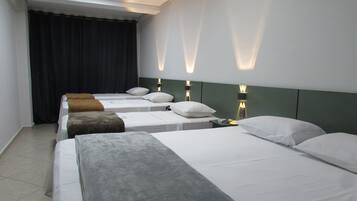 A hotel room with four single beds, each with a pillow and a blanket. There are wall-mounted lights above each bed.