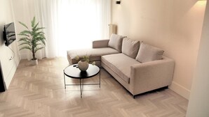 A modern living room with a beige sofa, a small round table with a vase, and a potted plant. - Citybreak Apartments 301 in Athens, Greece (Athens)