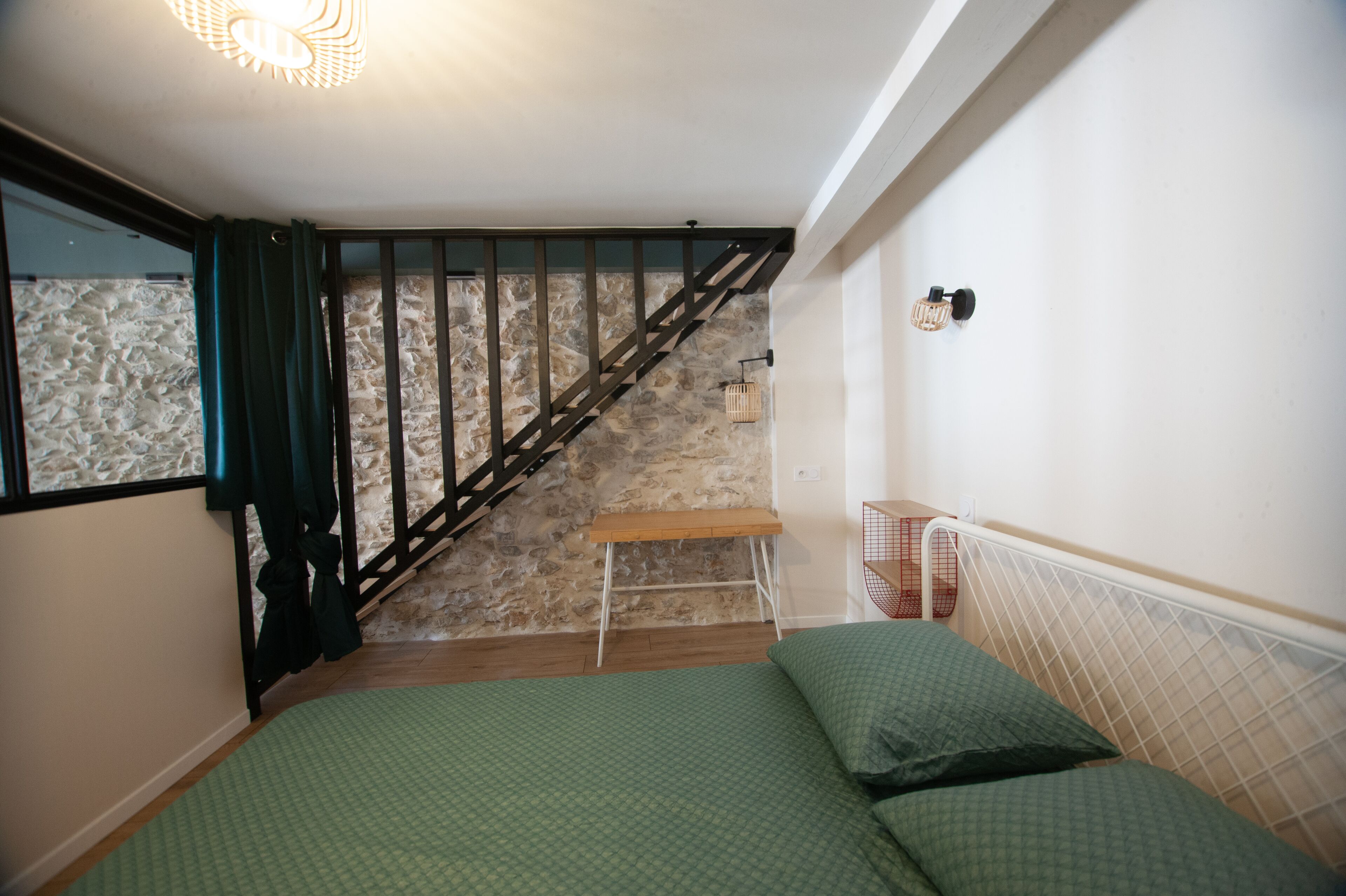 A bedroom with a bed, a wooden bench, a staircase, and a stone wall.
