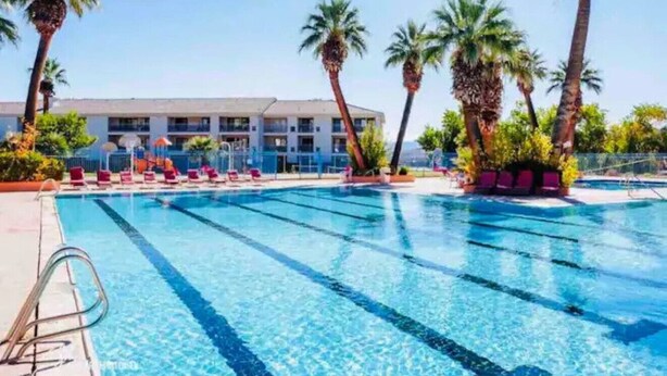 Ein Swimmingpool mit klarem, blauem Wasser, umgeben von Palmen und einem Gebäude mit mehreren Balkonen.