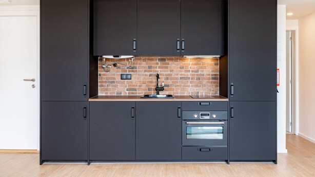 Una cocina moderna con armarios oscuros, un salpicadero de ladrillo y electrodomésticos integrados.