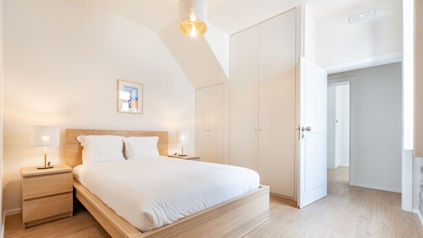 Une chambre à coucher avec un lit en bois, des tables de chevet, une lampe fixée au mur et une armoire.