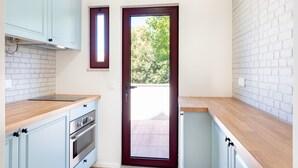 Une cuisine avec des meubles de couleur bleu clair, un plan de travail en bois et une porte à cadre rouge donnant sur un balcon.