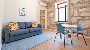 Un salon moderne avec un canapé gris, des coussins colorés, un tapis bleu et un coin repas comprenant des chaises bleues et une table blanche.