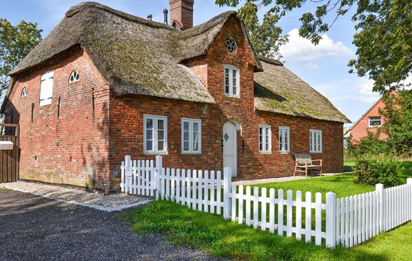 Una casa tradizionale in mattoni con tetto di paglia, recinzione in legno bianco e un piccolo giardino.