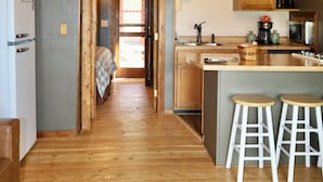 A cozy loft-style kitchen with wooden beams, a ceiling fan, and a central island with stools. - Moose Cabin - Mountain Views, Hear Rushing River, Private, Pet Friendly (Fishtail)